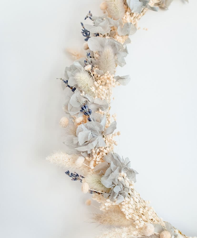 Rosa-Cadaques-couronne-bleue-fleurs-sechees couronne de fleurs séchées accrochée au mur dans les tons bleu-gris avec de l'hortensia bleu clair pour décorer les chambres d'enfants